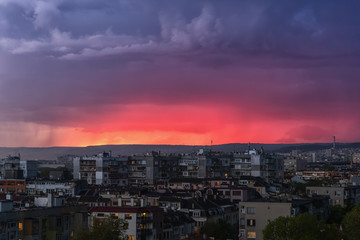 A storm is approaching the city in the late evening. Gleams of distant lightning reddened the sky above the hills outside the city. Scenic cityscape just before the storm.