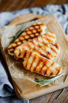 halloumi cheese with rosemary on a wooden cutting board on wooden table