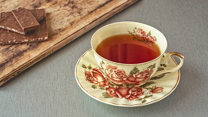 a beautiful Cup of tea with a picture of roses on a gray table against a background of chocolate pieces