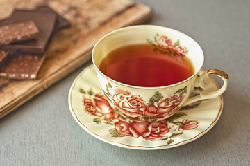 a beautiful Cup of tea with a picture of roses on a gray table against a background of chocolate pieces