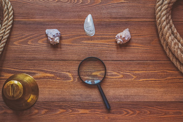 Shells, magnifying glass, bell and rope against dark brown wooden boards as background texture.