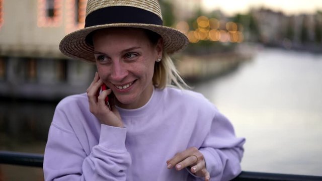 Close up view of cheerful caucasian female tourist enjoying mobile conversation while sitting outdoors, happy smiling hipster girl calling online via smartphone application using roaming connection
