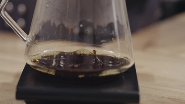 Drops of freshly made coffee drip into a glass jar on a wooden table. Full HD video, 240fps, 1080p.
