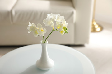 Beautiful white freesia flowers on table in light room, space for text