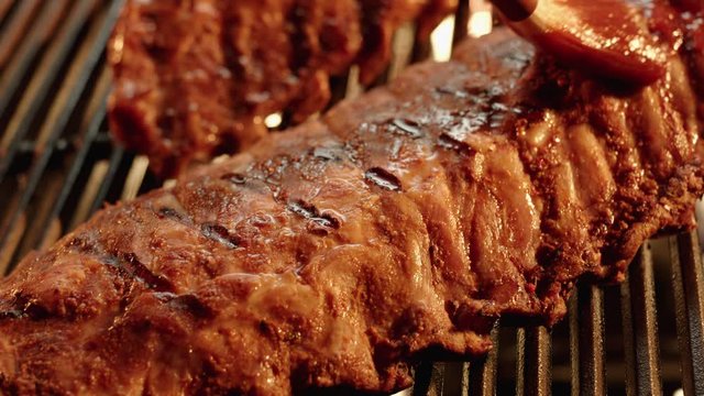 Ribs are basted with barbecue sauce on flaming grill in close up