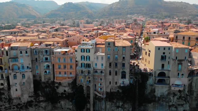 Aerial, pull back, drone shot of buildings on a steep cliff and the beach, on the coast of Tropea, sunny day, in Vibo Valentia, Calabria, south Italy.