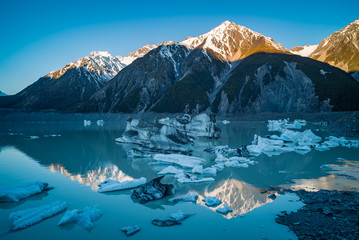 Late afternoon reflections of mountain peaks in turquoise melted glacier water filled with icebergs...