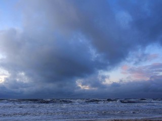 North Sea beach in Kijkduin, the Netherlands, sunset time, dramatic clouds, subtle red clouds, rain clouds, rough sea, dutch weather
