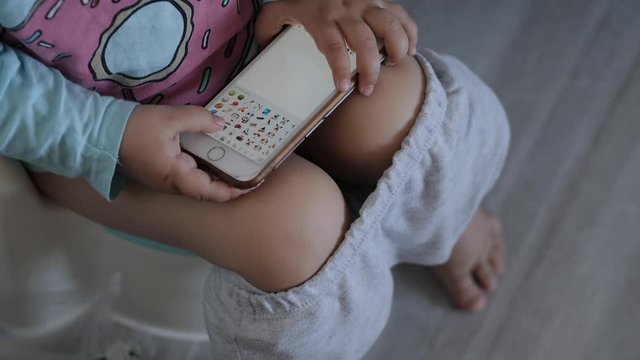 little girl sitting on the potty into the toilet with a smartphone in hand