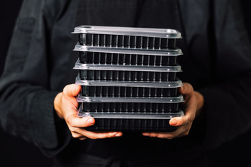 Chef holding in hands stack of plastic containers with food to take away 