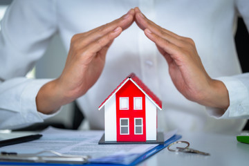 Red roof house Placed on the sales contract And have the hands of a businessman or an agent protecting the house, the idea of home insurance, investing, renting or buying Real Estate and Mortgages.