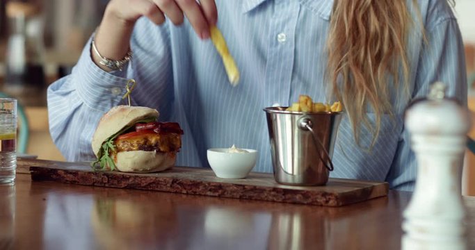 Close up burger and blonde woman dipping fries on mayo