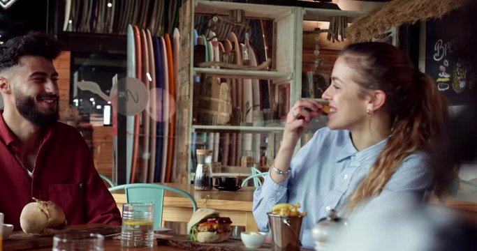 Young middle-eastern man feeding frie to blonde friend at restaurant