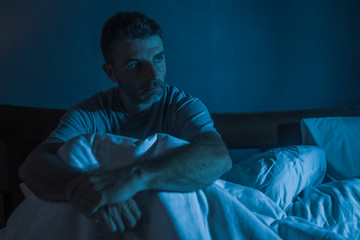 dramatic portrait in the dark of attractive depressed and worried man on bed suffering depression...