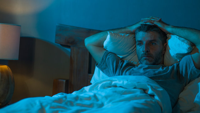 dramatic portrait in the dark of attractive depressed and worried man on bed suffering depression crisis and anxiety feeling lost lying sleepless in insomnia and life problem concept