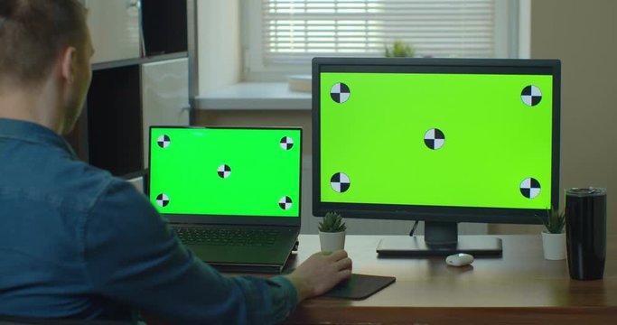 Designer Sitting at His Desk Uses Desktop Computer with Green Mock-up Screen.