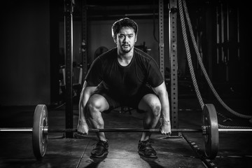 Fototapeta na wymiar asian strong athletic man having workout and bodybuilding with barbells weight lift clean setting style in gym and fitness club in dark tone black and white