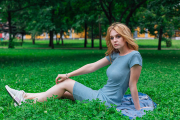 Naklejka na ściany i meble Portrait of a young beautiful woman, sitting on the green grass in city park.
