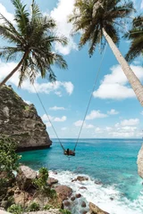 Foto op Aluminium Young girl swinging on a swing overlooking the blue sea. Travel adventure on paradise tropical island Nusa Penida. A young girl swinging on a swing between palm trees on the beach of a tropical island © Yevhenii