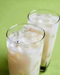 Cold soy milk in the glass with ice and green background 