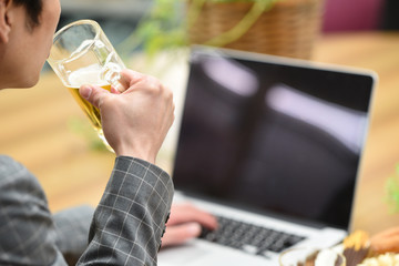 パソコンを見ながらビールを飲む男性