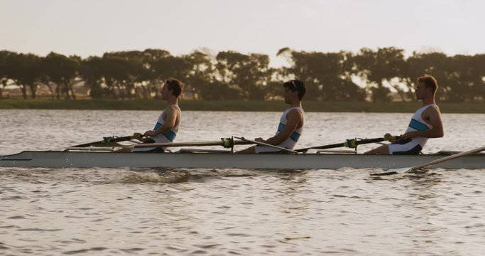 Side view of male rower team rowing on the lake