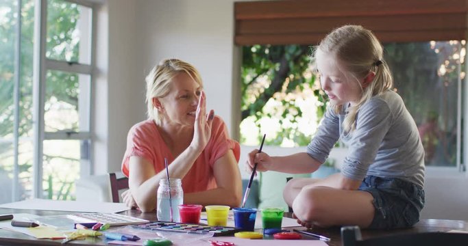 Side view of Caucasian woman painting with her daughter at home and giving a high five