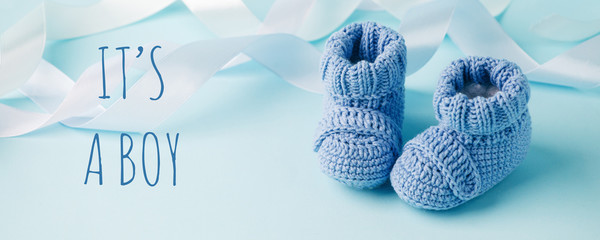 It's a boy text. Blue Baby knitted shoes for newborns on blue background, Minimal baby shower, newborn party background, copy space - 345466536