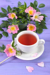 Fototapeta na wymiar Cup of tea and wild rose flower on purple boards