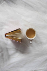 Top view of the cup of coffee and a standing book beside it on a white tulle fabric background
