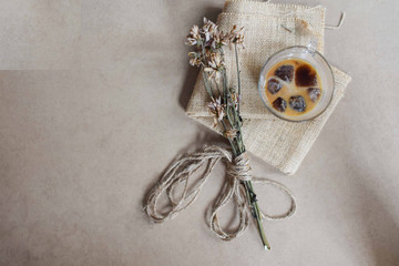 Flat lay of dried flowers and an iced coffee sitting on a piece of a brown burlap sack. Earth toned background.