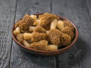 A clay plate with fresh morels on a wooden table.