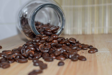 Coffee beans spilled from a transparent jar on wooden texture background. Conceptual image of coffee with copy space. Still life image
