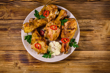 Baked chicken legs with parsley, garlic and sliced red hot pepper in a plate. Top view