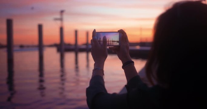 Hipster woman taking photos of landscape on smartphone at sunset