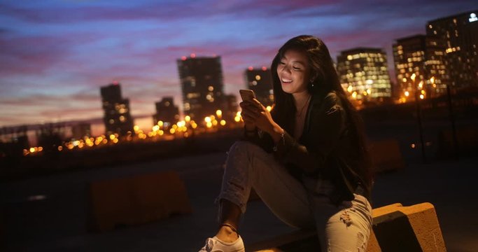 Hipster Asian teenage girl chatting online using smartphone in city