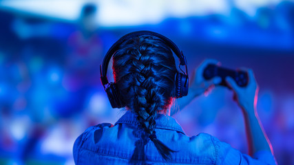 A gamer or a streamer girl at home in a dark room with a gamepad playing with friends on the networks in video games. A young man sits in front of a monitor or TV. © Anton