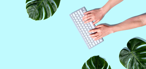 Person using a computer keyboard with tropical leaves from above