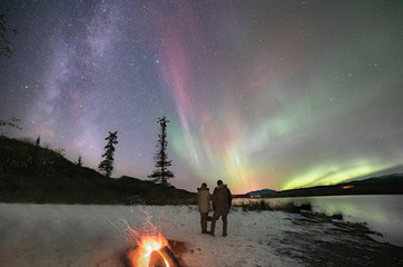 Couple standing admiring the northern lights & milky way in Yukon Territory, northern Canada taken...