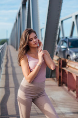 Pretty young woman posing on the old rusty transport bridge over the river during sunset.
