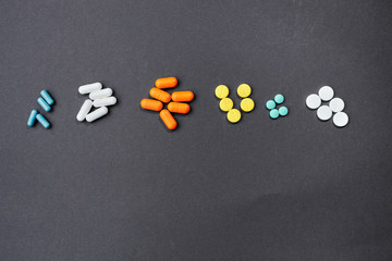 several handfuls of multicolored tablets lie in a row against a gray background. top view. place for sign