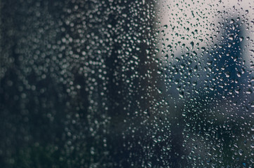 Naklejka na ściany i meble Blurred and focus of rain drop on glass window in monsoon season with blurred building background for abstract and background concept.