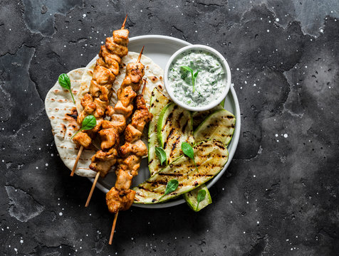 Chicken skewers souvlaki, grilled zucchini, tortillas and tzadziki sauce - delicious greek style lunch on a dark background, top view