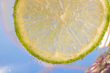 macrophotography of a lemon slice in cold carbonated water with blue sky background