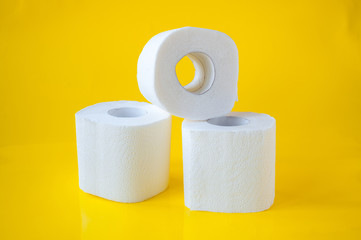 Three rolls of white toilet paper on a yellow background