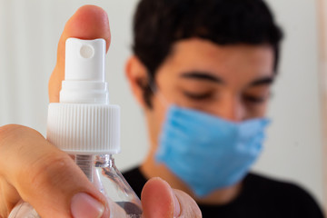 young man wearing a blue medical mask holding a bottle of disinfectant spray