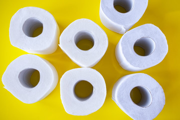 Pile of rolls of white toilet paper on a yellow background, top view