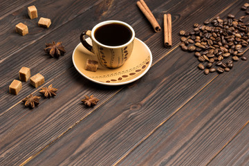 Cup of coffee. Coffee beans scattered on table, star anise and pieces of brown sugar.