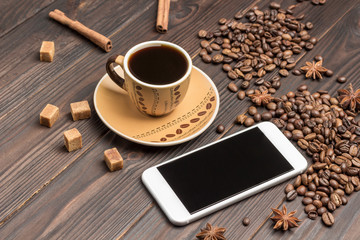 Smartphone, сup of coffee. Coffee beans scattered on table, star anise and pieces of brown sugar.