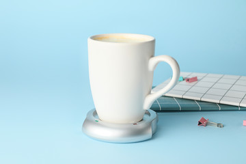Cup of coffee with heater on color background